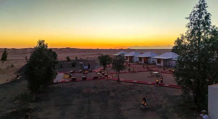 Desert camp with white tents and lantern-lit paths at sunset, with the Erg Chebbi dunes behind