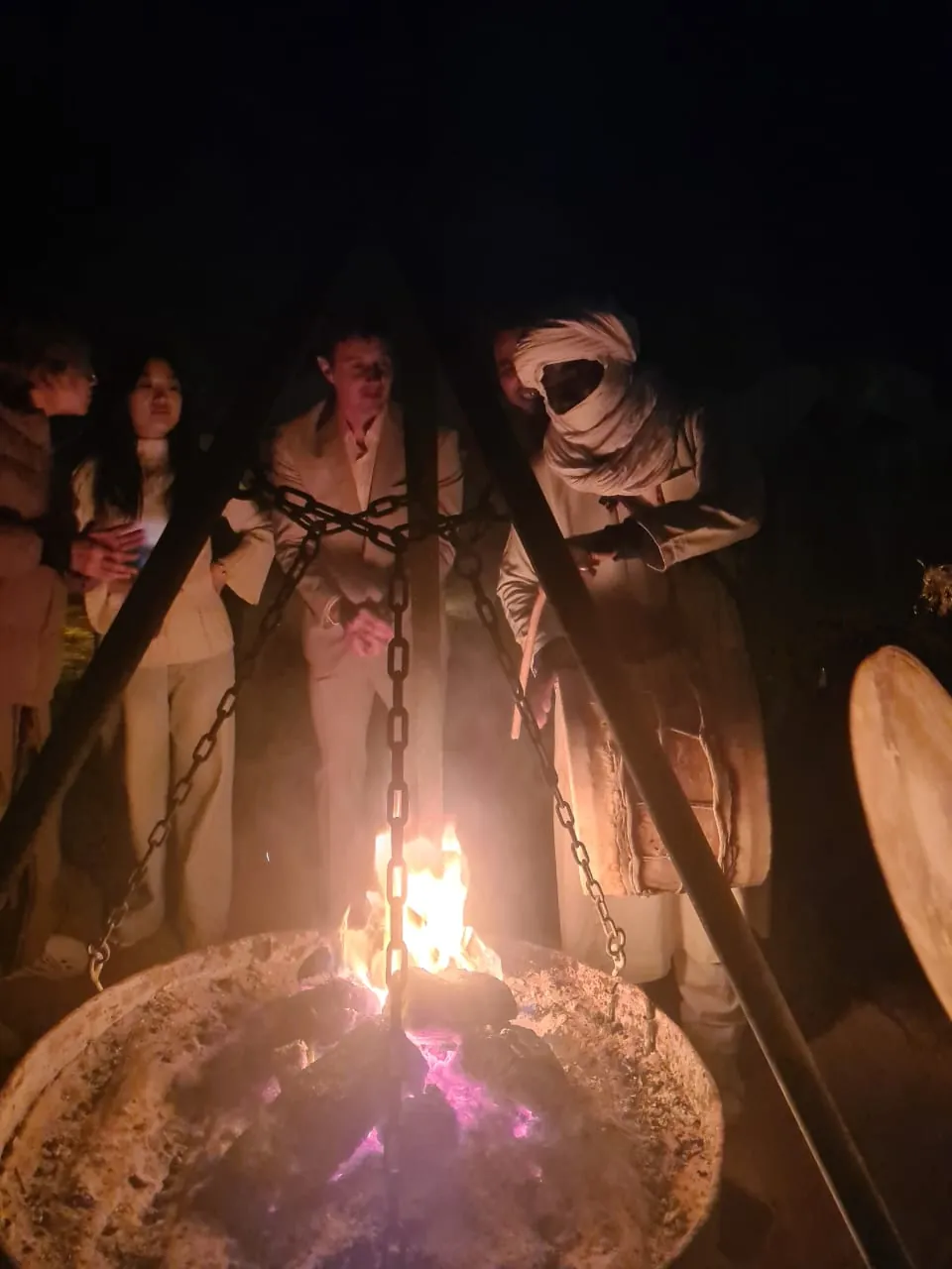 Musician in a white turban beside the campfire at night with guests listening