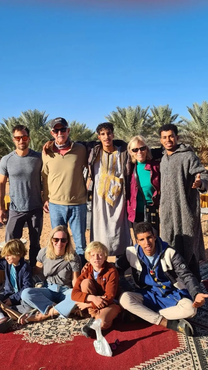 A group of guests with the camp team on carpets in front of palm trees