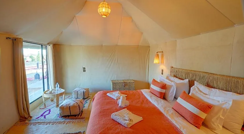 Double bed with terracotta throw inside a desert tent with a large window